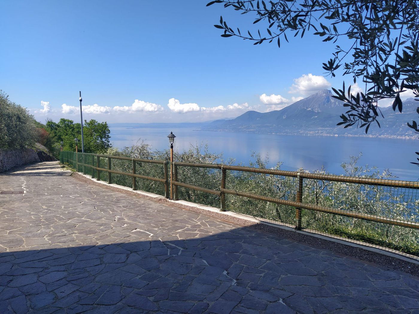 Una strada interna pavimentata che corre lungo la tenuta, con una staccionata in legno e il lago sotto.