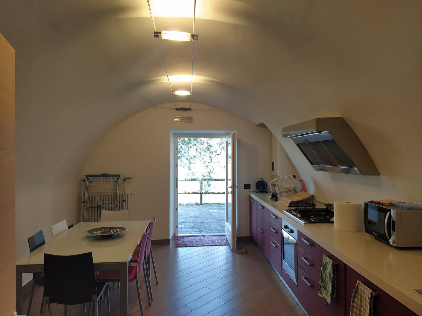 La seconda cucina, sotto una volta a botte, con un tavolo lungo e una porta aperta sulla luce esterna.